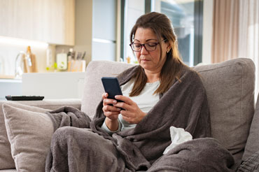 Woman covered with blanket sitting on couch reading her phone