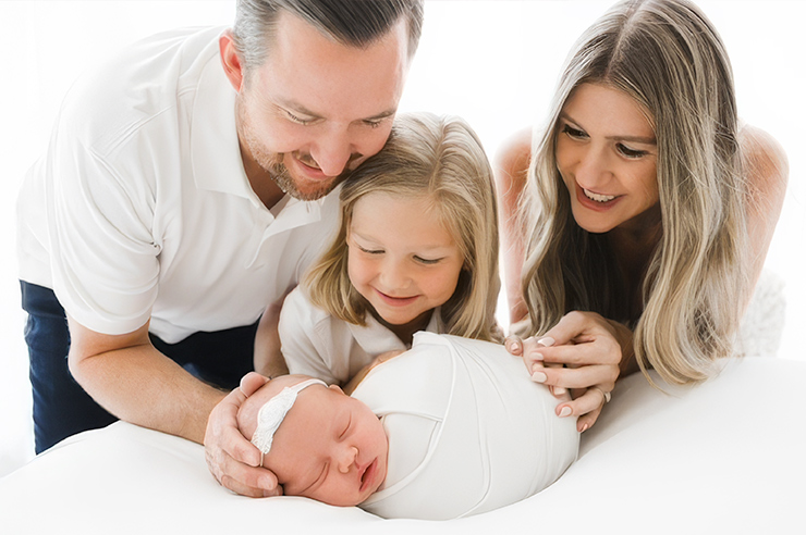 Father, Mother and daughter gather around their new infant child.