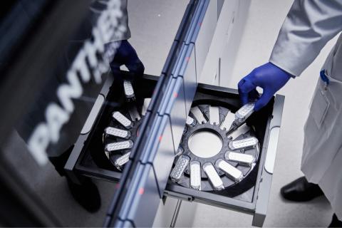 Lab technician's hand places a cartridge into a tray to be tested in a lab setting.