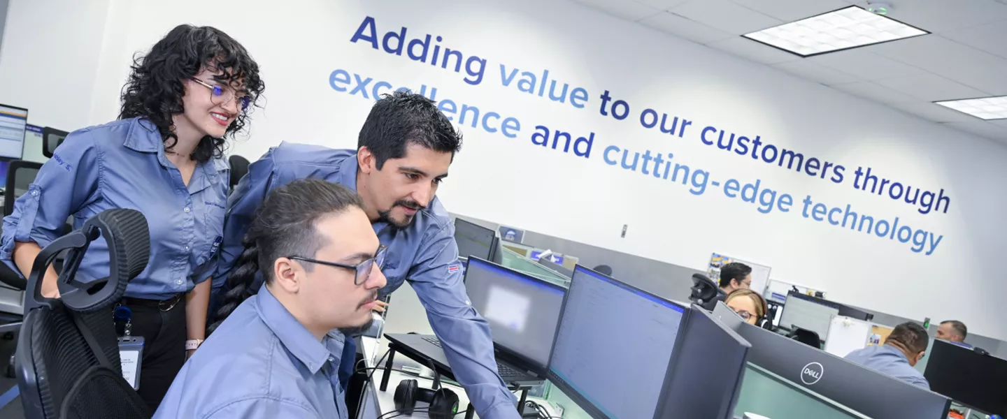 Coworkers grouped together and looking at a monitor in an office setting.