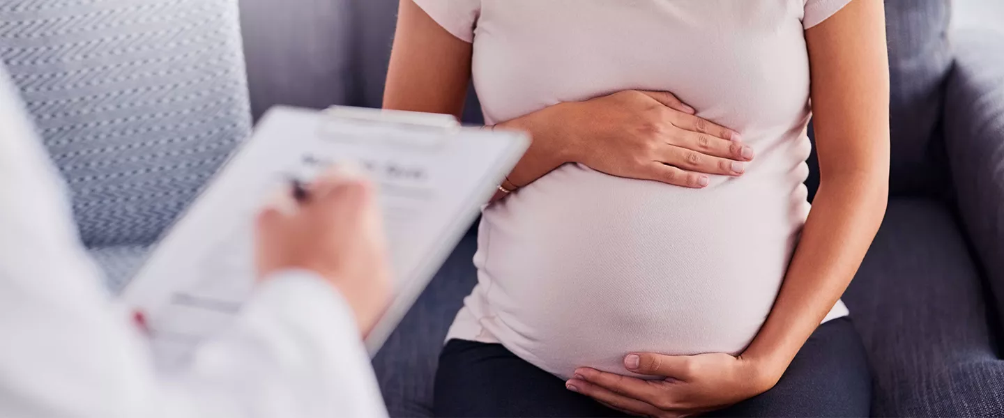 Pregnant woman holding stomach and talking to health provider.