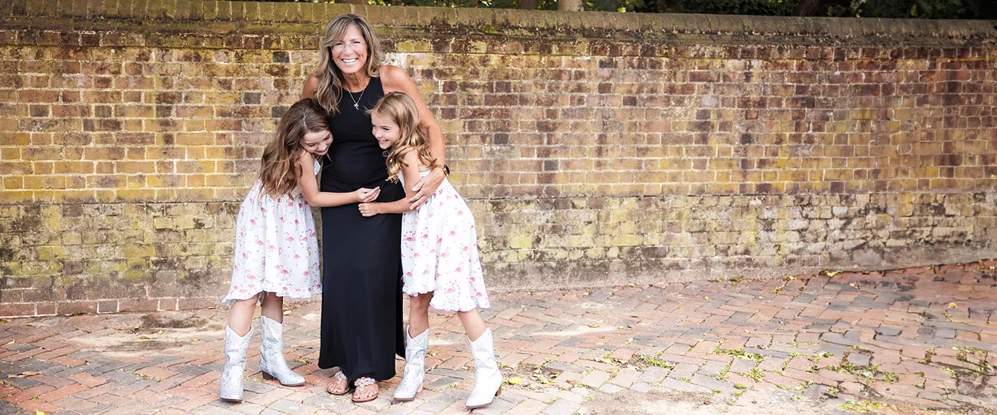 Woman hugging children grouped in front of brick wall.