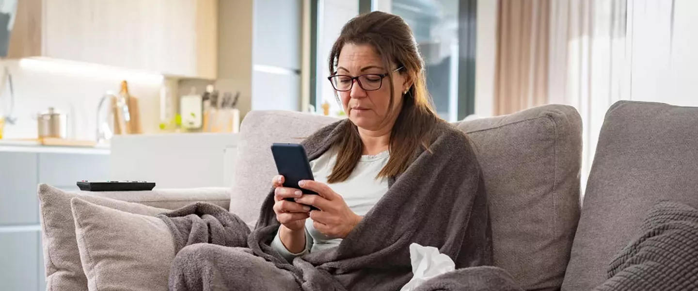 Woman covered with blanket sitting on couch reading her phone